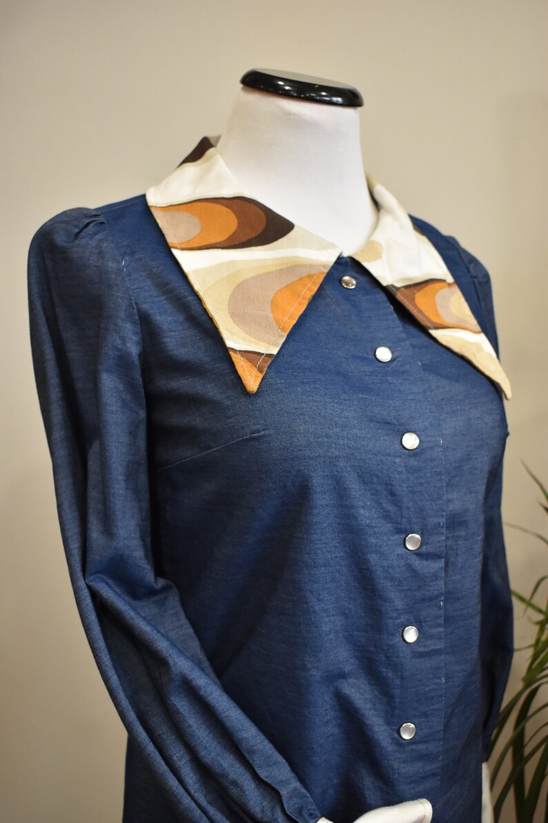 May include: A blue denim shirt with a large, white collar featuring a brown and beige geometric pattern.