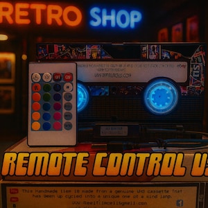 a remote control USB device, which is a handmade item made from a genuine VU cassette tape. The device has been upcycled into a unique one at a kind lamp. The remote control USB is displayed on top of a stack of books, with a neon sign reading "RETRO SHOP" in the background.