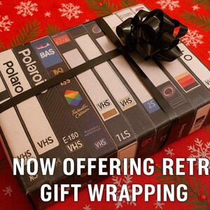 A gift wrapped in a black ribbon with a bow, featuring a collection of VHS tapes on the wrapping paper.