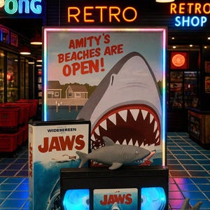 a promotional display for the movie "Jaws", including a shark-themed poster, a DVD case, and a shark plush toy.