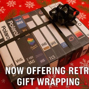 A gift wrapped in a black ribbon with a bow, featuring a collection of VHS tapes on the wrapping paper.