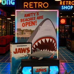 a promotional display for the movie "Jaws", including a shark-themed poster, a DVD case, and a shark plush toy.
