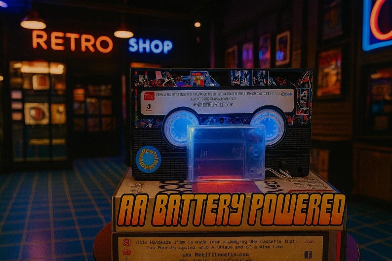 a retro-style cassette tape and a battery-powered cassette tape, both displayed in a dimly lit room with neon signs in the background.