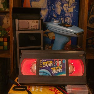 a Star Trek video tape, a vintage electronic device, and a Star Trek poster on a shelf.
