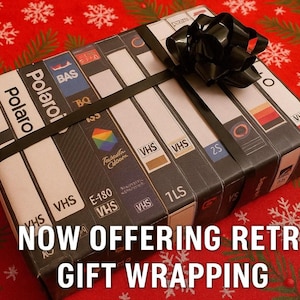 A gift wrapped in a black ribbon with a bow, featuring a collection of VHS tapes on the wrapping paper.