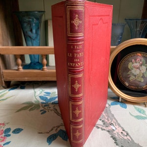 May include: A red leather-bound book with gold accents and the title "G. Fath Le Paris des Enfants" on the spine.