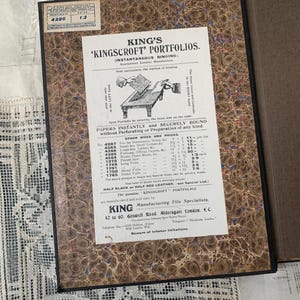 May include: An antique King's 'Kingscroft' Portfolio with instantaneous binding. The cover has a marbled design in shades of brown, blue, and cream. The interior shows a printed advertisement with text and illustrations.