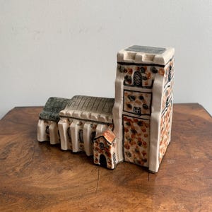 May include: A ceramic church figurine with a rectangular tower and a pitched roof. The tower has brown and orange speckled details. The roof is gray, and the walls are white with black trim. A small building with a red roof is attached.