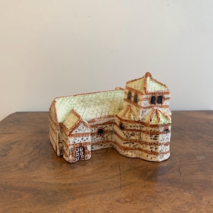 May include: A ceramic model of a church with a light green roof and a tan and brown exterior. The building has multiple windows and a detailed architectural design. The model is placed on a wooden surface.