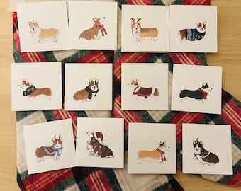 May include: A collection of square greeting cards featuring watercolor illustrations of corgi dogs in festive attire. Each card showcases a different corgi, adorned with holiday accessories like scarves, sweaters, and antlers, set against a white background.
