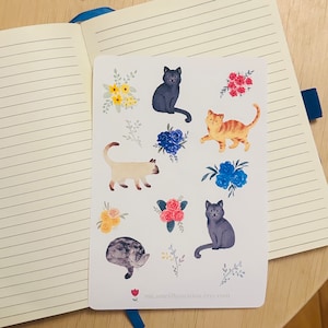 May include: A sheet of stickers featuring colorful cats and flowers. The cats are in various poses, including sitting, lying down, and walking. The flowers are in a variety of colors, including pink, blue, yellow, and red.