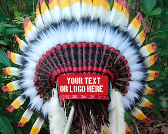 Op de afbeelding: Een decoratieve verentooi met een cirkelvormige opstelling van witte, gele en rood getipte veren. Een centrale rode band toont de tekst "YOUR TEXT OR LOGO HERE" in het wit. De tooi bevat witte bontaccenten en bruine franjes aan de onderzijde.