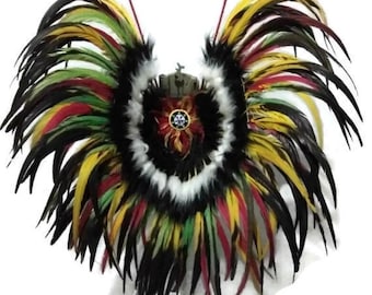 May include: A large, fan-shaped decorative headpiece constructed from layered feathers in vibrant shades of yellow, green, red, and black. The center features a circular emblem with a geometric pattern, surrounded by a dense ring of white feathers.