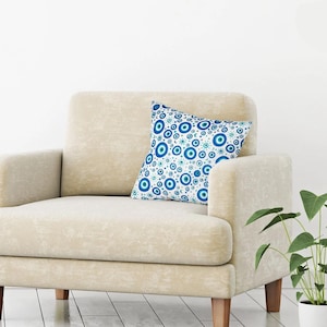 May include: A white armchair with a blue and white patterned throw pillow featuring a repeating design of evil eye charms.