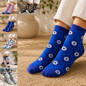 May include: A collection of six pairs of crew socks featuring various patterns including blue evil eyes on a blue background, white evil eyes on a white background, pink hamsa hands, and black celestial motifs with white and gold accents.