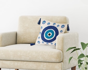 May include: A white throw pillow with a blue and turquoise evil eye design. The pillow has tassels on each corner.