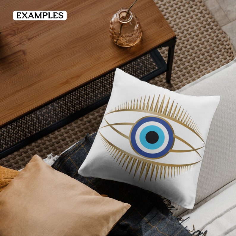May include: A square white throw pillow featuring a centered graphic of a stylized eye. The design includes a central black pupil, a light blue iris, and a dark blue outer ring, all surrounded by long, pointed gold eyelashes and eye contours.
