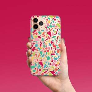 May include: A clear phone case with a colorful terrazzo pattern. The case has a "Talk & Tell" logo in the bottom right corner.