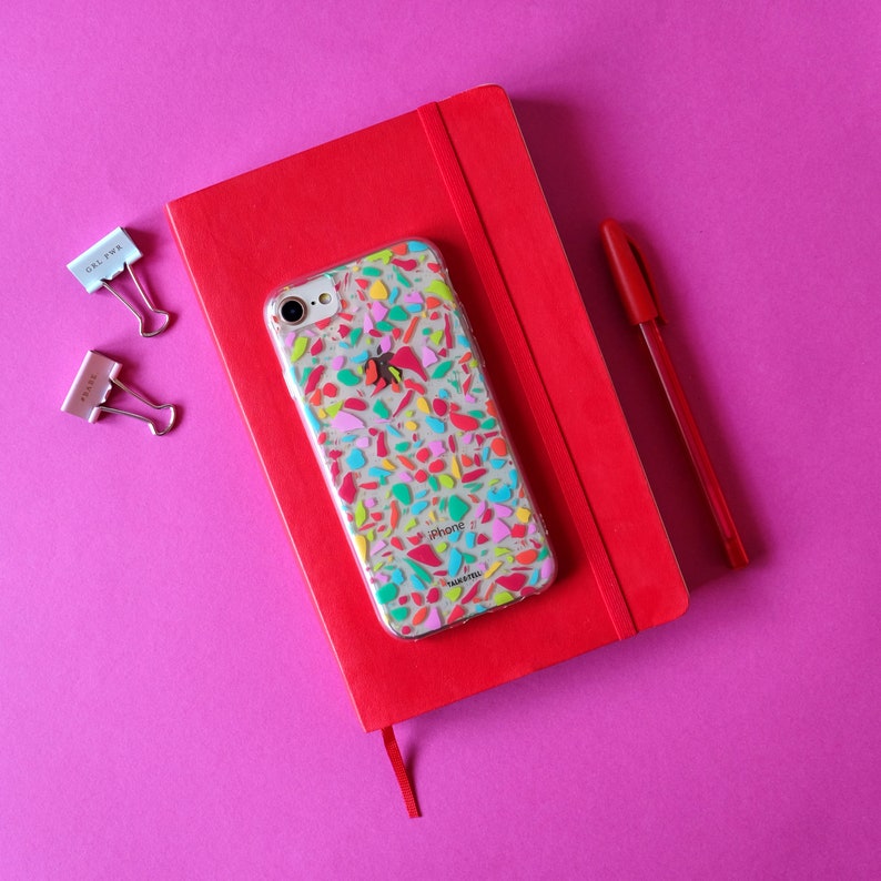 May include: A red notebook with a clear phone case with a colorful mosaic design. The phone case has the word "iPhone" printed on it.