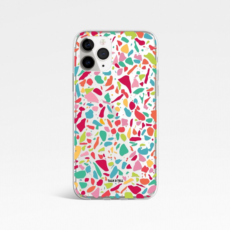 May include: A clear phone case with a colorful terrazzo pattern. The case has a white background with red, pink, blue, green, yellow, and orange terrazzo pieces. The case has the text "TALK & TELL" printed on the bottom.