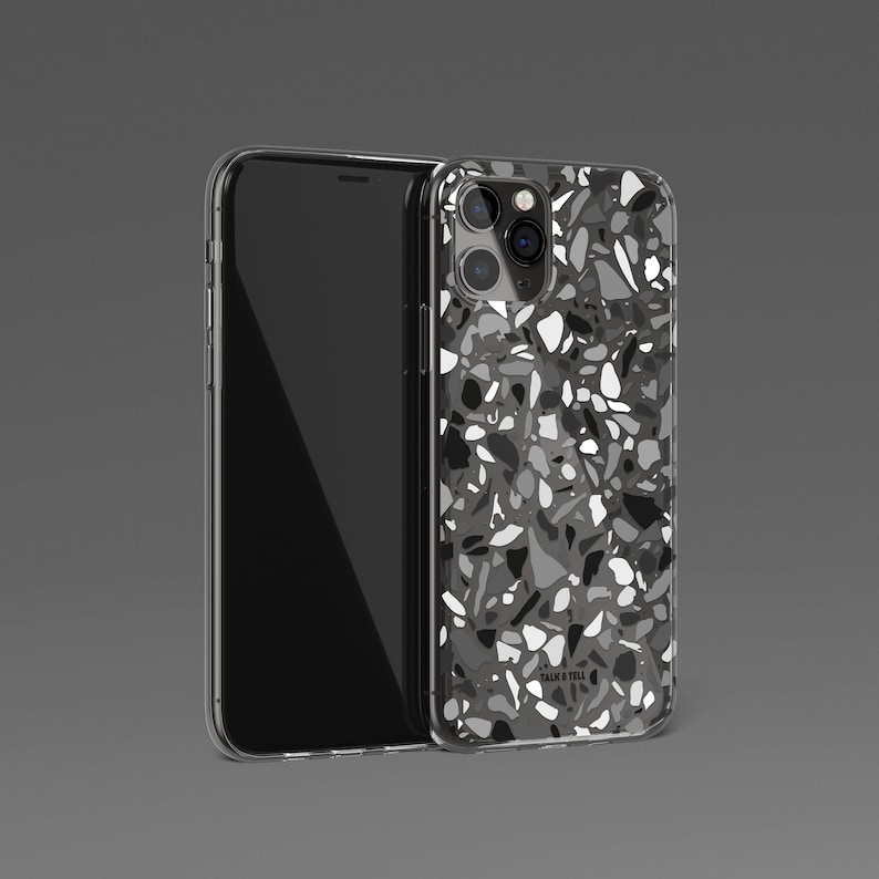 May include: A clear phone case with a black and white terrazzo pattern. The case has a raised camera bump and the text "Talis & Tell" is printed on the back.