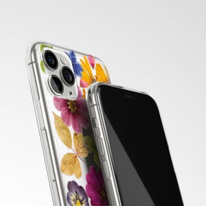 Może przedstawiać: Przezroczyste etui na telefon z kwiatowym wzorem z suszonych kwiat&oacute;w w odcieniach ż&oacute;łtego, r&oacute;żowego, niebieskiego i zielonego. Etui jest pokazane na czarnym iPhonie.