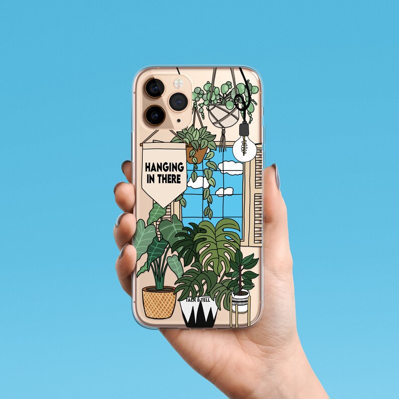 May include: A phone case featuring a colourful illustration of hanging plants and a window with a blue sky. The text "HANGING IN THERE" is on a banner in the illustration.