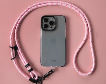 May include: A pink and white patterned phone strap with a black phone case and a clear back. The phone case has a black camera bump with four lenses. The text "TAKE IT TELL" is printed on the back of the case.