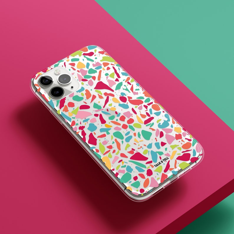 May include: A clear phone case with a colorful terrazzo pattern. The case has a white background with multi-colored chips of various sizes and shapes. The case has a camera cutout and the text "Talk & Tell" printed on the bottom right corner.