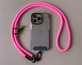 May include: A clear phone case with a black border and a bright pink lanyard. The lanyard is made of a thick, woven material and has black metal clasps. The phone case has a silver Apple logo on the back.