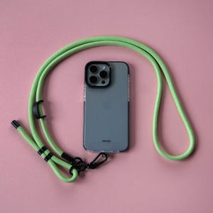 Może przedstawiać: Jasnozielony pasek do telefonu z czarnym klipsem i czarną i srebrną obudową telefonu. Obudowa telefonu ma obiektyw aparatu z czterema czarnymi kółkami.