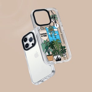 May include: A clear phone case with a colourful design featuring plants and the text "Hanging in There". The case is designed for an iPhone with a camera bump.