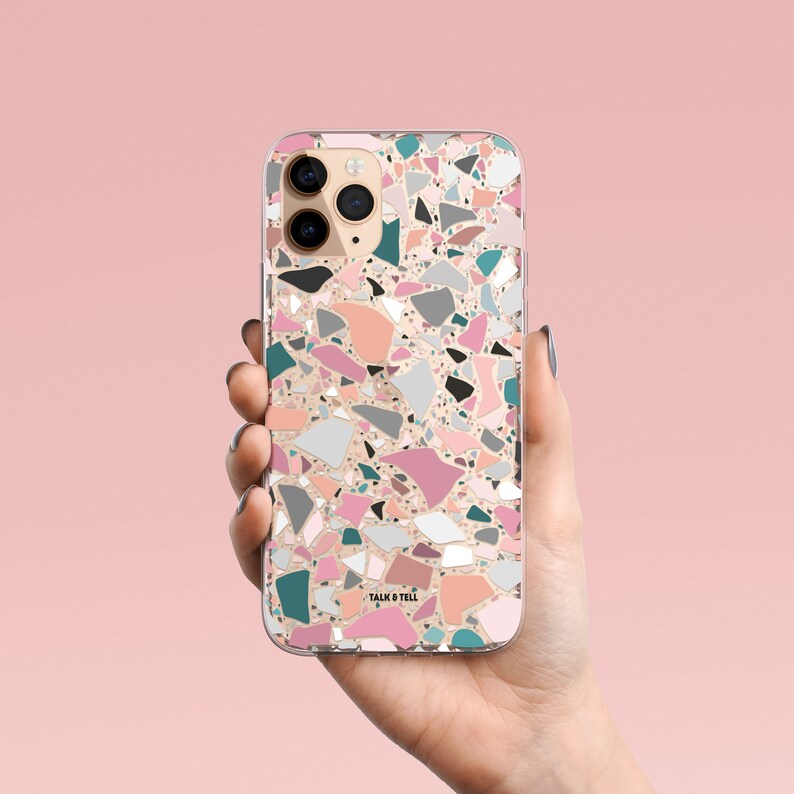 K&ouml;nnte beinhalten: Eine transparente Handyh&uuml;lle mit Terrazzo-Design. Die H&uuml;lle zeigt ein Muster aus unregelm&auml;&szlig;igen Formen in Rosa, Grau, T&uuml;rkis und Schwarz auf hellpfirsichfarbenem Hintergrund. Die Worte "TALK & TELL" sind unten aufgedruckt.