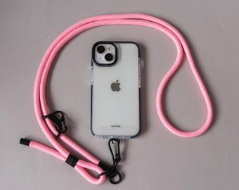 May include: A clear phone case with a black border and a pink lanyard. The phone case has a black camera ring and a silver Apple logo. The pink lanyard is made of a thick, woven material and has black hardware.