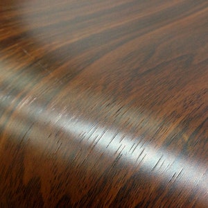 May include: Close-up of a dark brown woodgrain surface with a slight sheen. The surface is smooth and appears to be made of laminate.