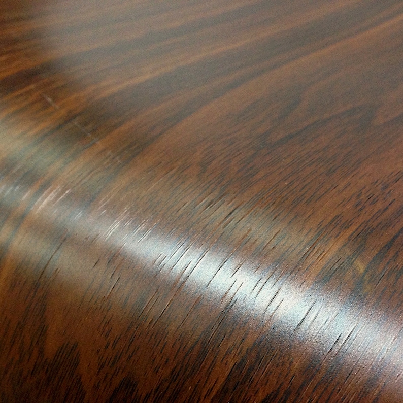 May include: Close-up of a dark brown woodgrain surface with a slight sheen. The surface is smooth and appears to be made of laminate.
