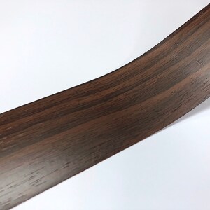 May include: A close-up of a dark brown woodgrain vinyl contact paper. The paper has a realistic woodgrain pattern.