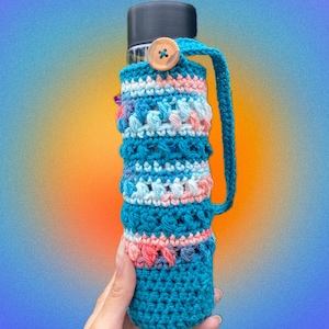 May include: A teal blue crocheted bottle cozy with a pink, white, and blue striped pattern. The cozy has a brown button and a long strap.