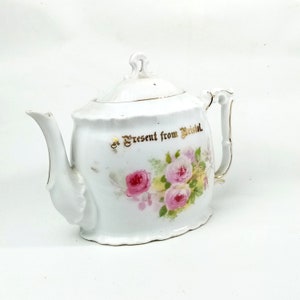 Puede incluir: Tetera de porcelana blanca con ribete dorado y diseño floral. La tetera tiene tapa y asa. El texto "A Present from Bristol" está escrito en dorado en el lateral de la tetera.
