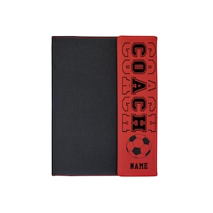 May include: Red leather binder with a black zipper and a black and white soccer ball graphic. The text "COACH" is written vertically in black on the front of the binder.