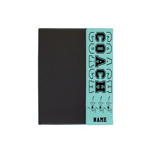May include: A teal blue notebook with a black and white graphic of a swimmer and the word "COACH" on the front. The notebook has a black cover.