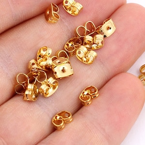 May include: A large quantity of gold-coloured earring backs. The backs are made of metal and have a double-prong design.