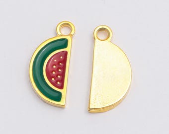 May include: Two semi-circular metal charms with gold-toned edges and loops. One charm features a red and green enamel watermelon slice design with small white dots, while the other charm is a plain, solid gold-toned semi-circle.
