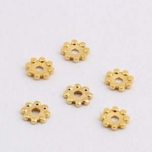May include: Six gold-colored metal spacer beads with a circular design. Each bead has a small hole in the center.