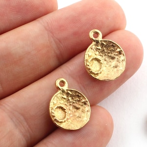 May include: Two gold-toned metal charms shaped like a moon with a textured surface and a small circle in the center. Each charm has a loop at the top for attaching to jewelry.