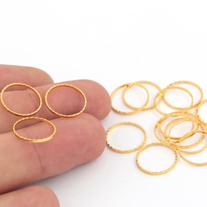 Op de afbeelding: Een groep gouden metalen sprongringen, sommige zijn op elkaar gestapeld en sommige worden in een hand gehouden.