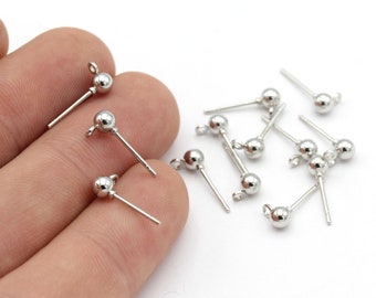 May include: A close-up of silver earring posts with round ball tops. The earring posts are scattered on a white surface.