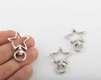 May include: Three silver star-shaped keyrings with a swivel clasp and a ring. The keyrings are on a white surface.