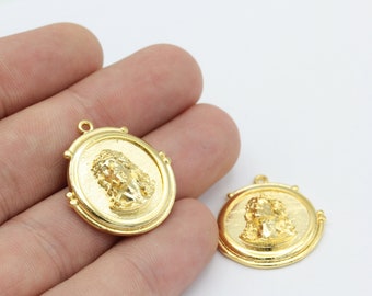 May include: Two gold-tone metal pendants featuring a raised image of a person's face. The pendants are round and have a decorative border.