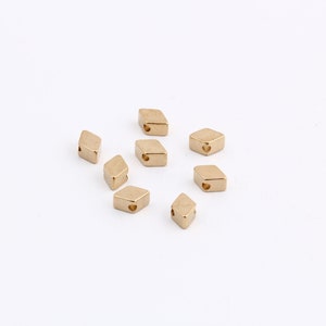 May include: A group of ten gold-colored metal diamond-shaped beads with a small hole in the center of each bead.
